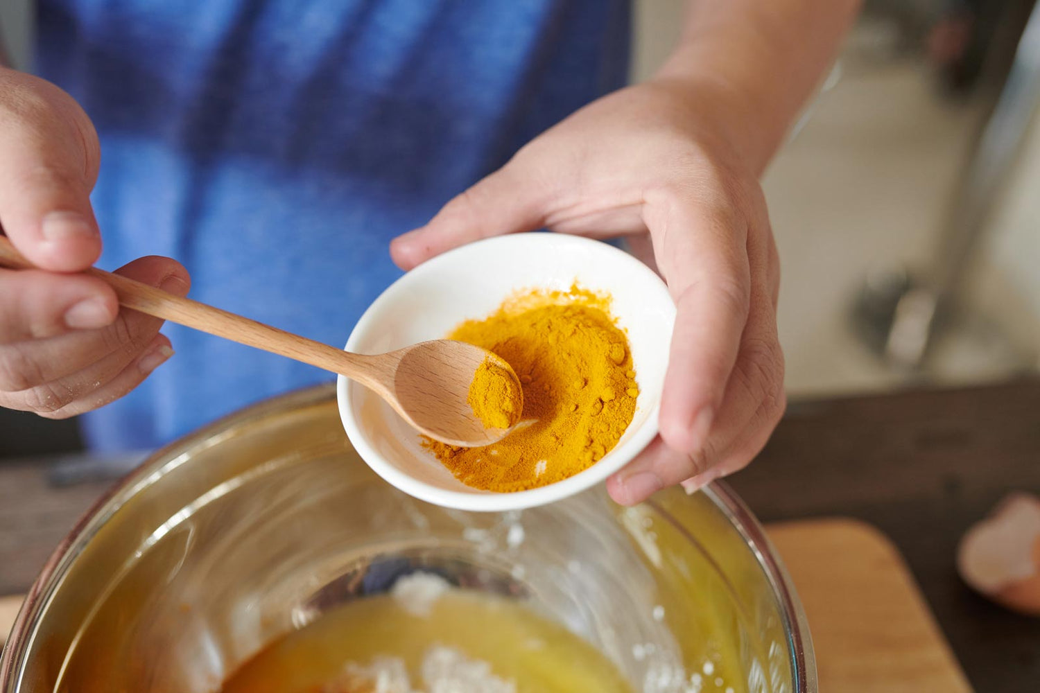 Hands spooning turmeric powder into a glass bowl of melted ghee to make turmeric gheeHands spooning turmeric powder into a glass bowl of melted ghee to make turmeric ghee
