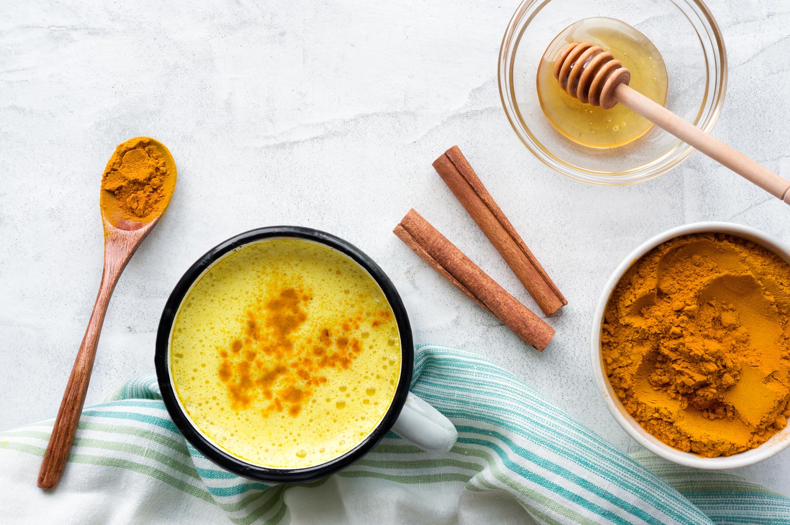 Golden milk latte with turmeric powder, cinnamon sticks, and honey on a marble surface