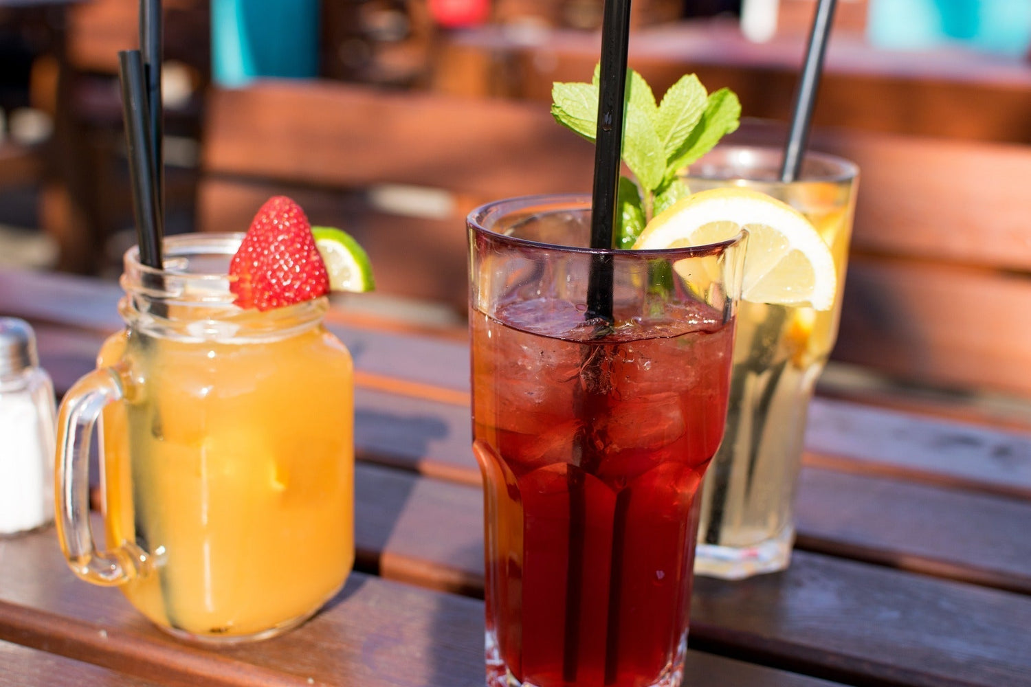 Three colorful loose leaf iced teas garnished with fresh mint lemon and strawberry served outdoors in summer