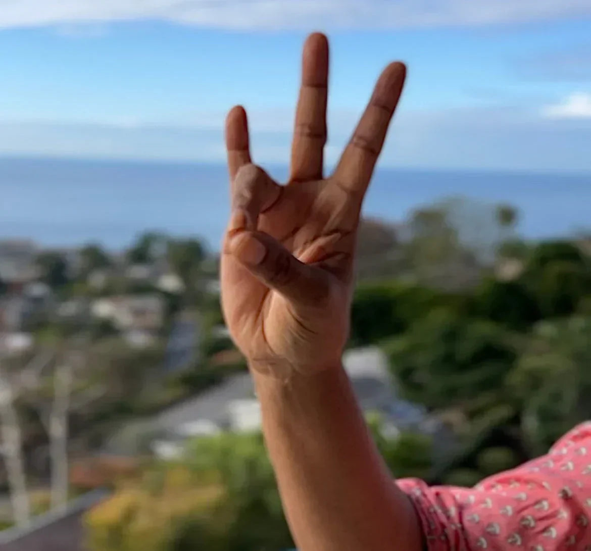Hand showing Peace Begins with Me Kundalini mudra gesture with Laguna Beach ocean view in background