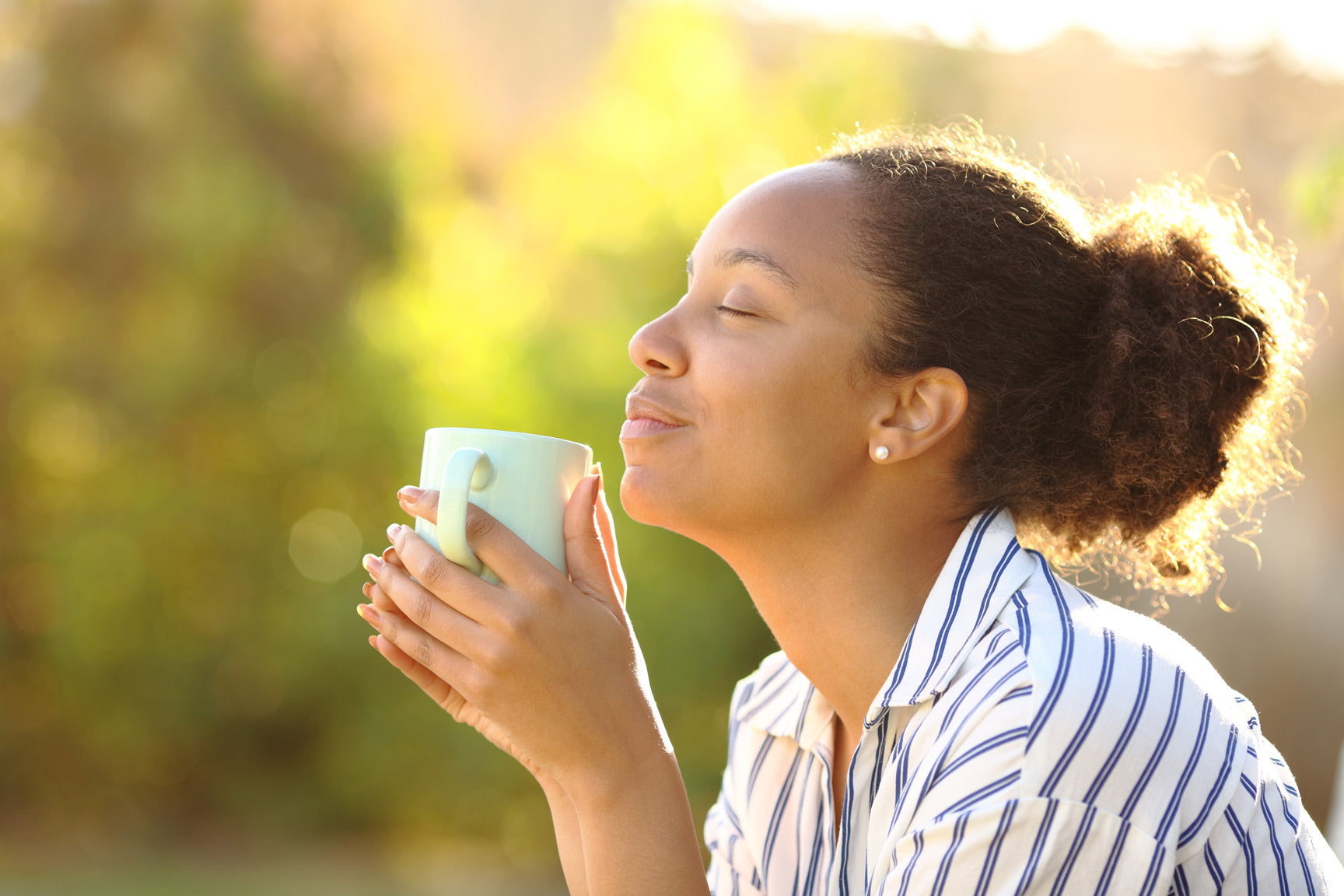 Woman breathing deeply and holding herbal tea cup outdoors in golden sunlight, Reiki stress relief practice Laguna Beach