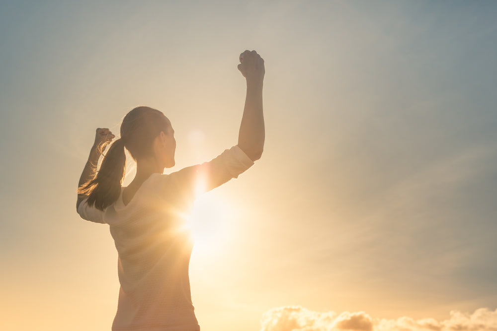 Woman with arms raised at sunrise practicing Ayurvedic morning routine to balance Vata dosha in winter